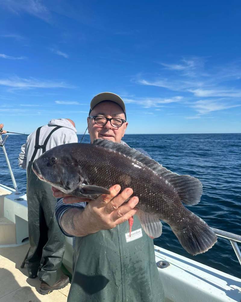 Smiling man on boat holding large fish under a clear blue sky.