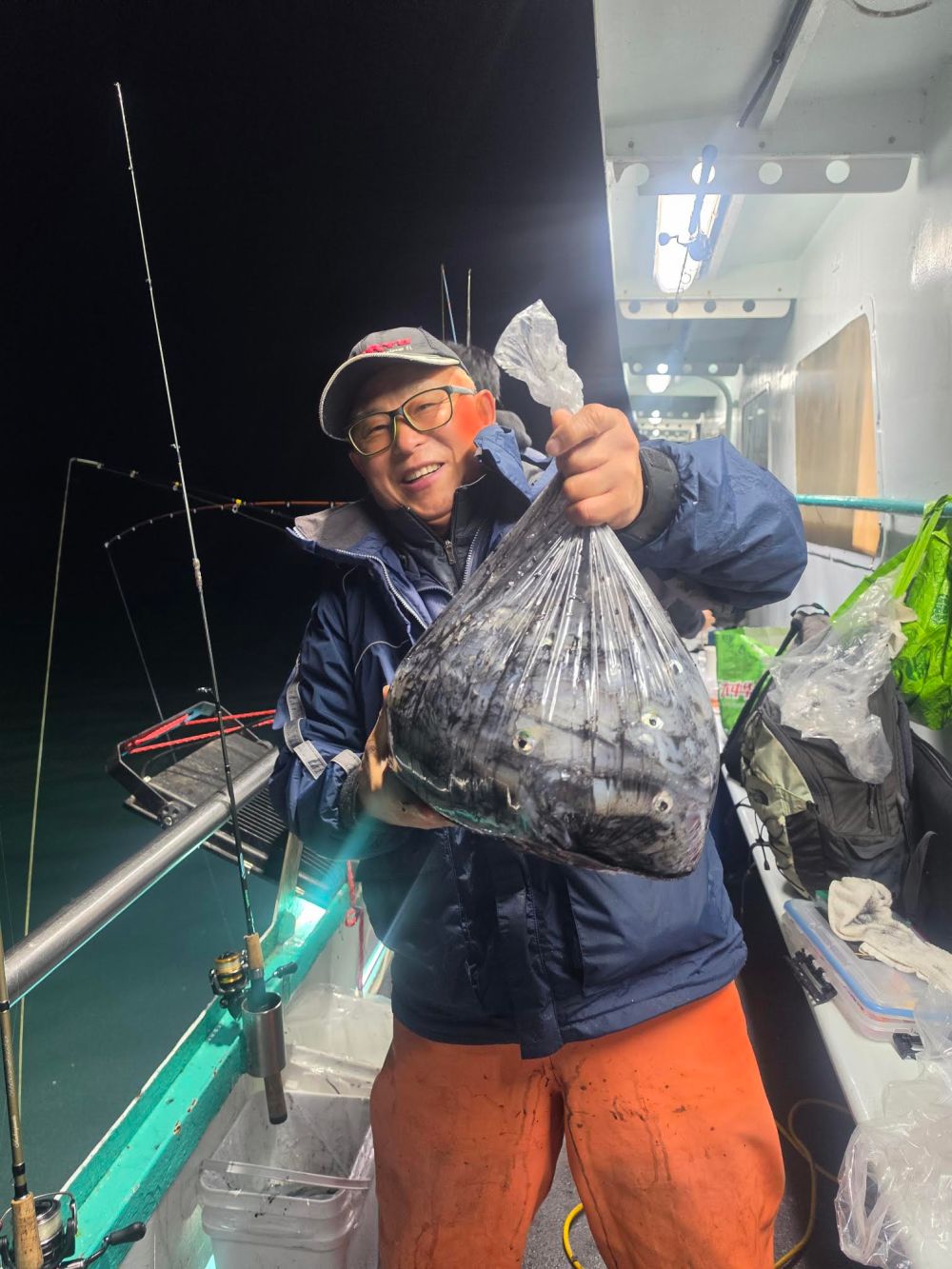 Person holding a large bag of fish on a boat at night.