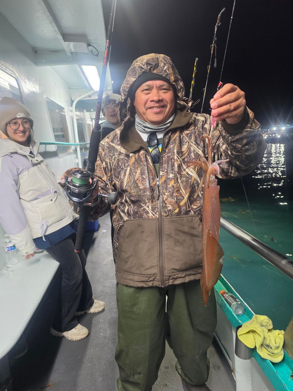 Man in camo jacket holds a catch on a boat at night.