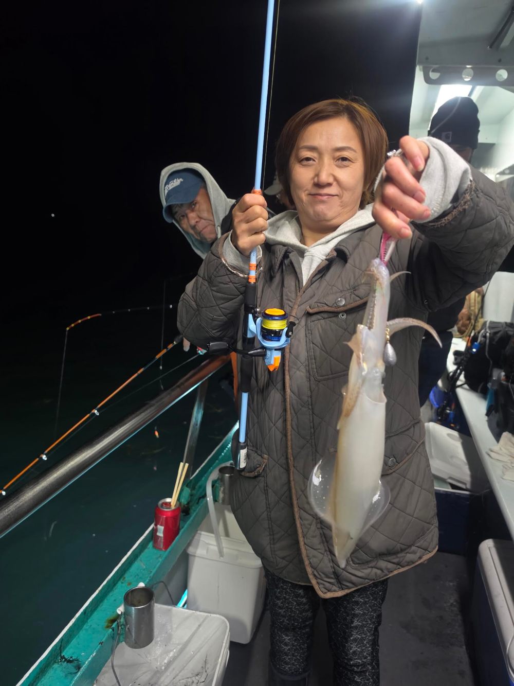 Person holding a squid on a fishing boat at night.