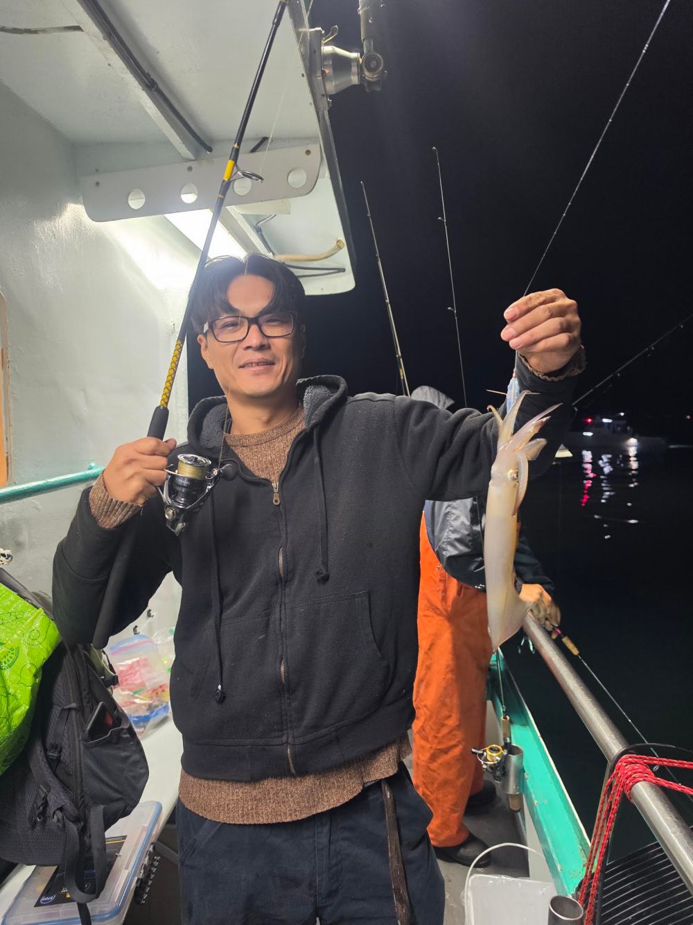 Person on boat holding a fishing rod and a caught squid at night.