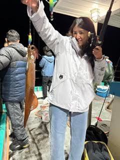 Person in a white jacket holding a fishing rod and catching a squid on a boat at night.