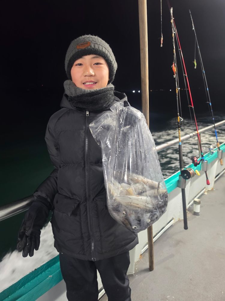 Child on a boat holding a bag of fish at night, with fishing rods in the background.