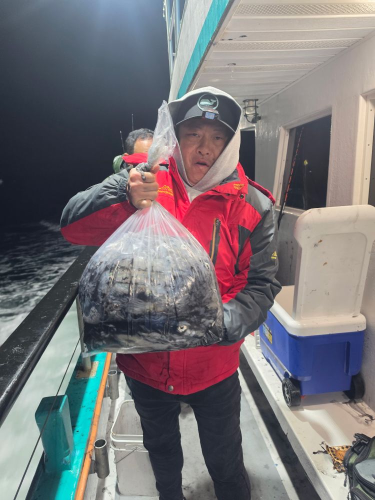 Person in red jacket holding a bag of fish on a boat at night.