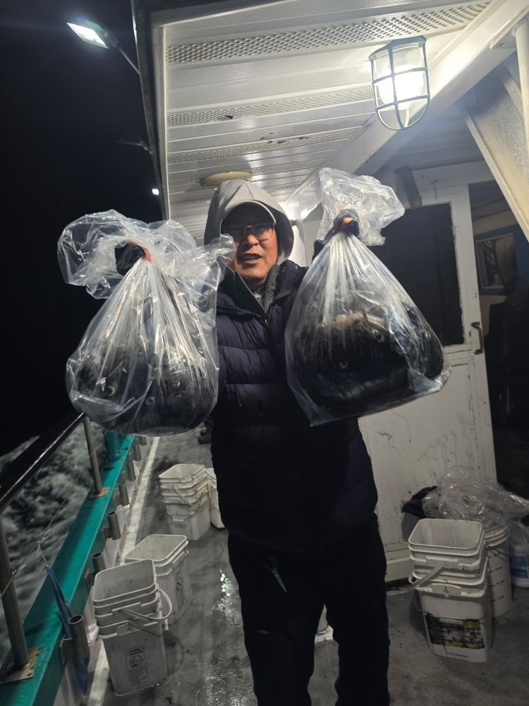Person on a boat holding two large bags, possibly containing fish, at night.