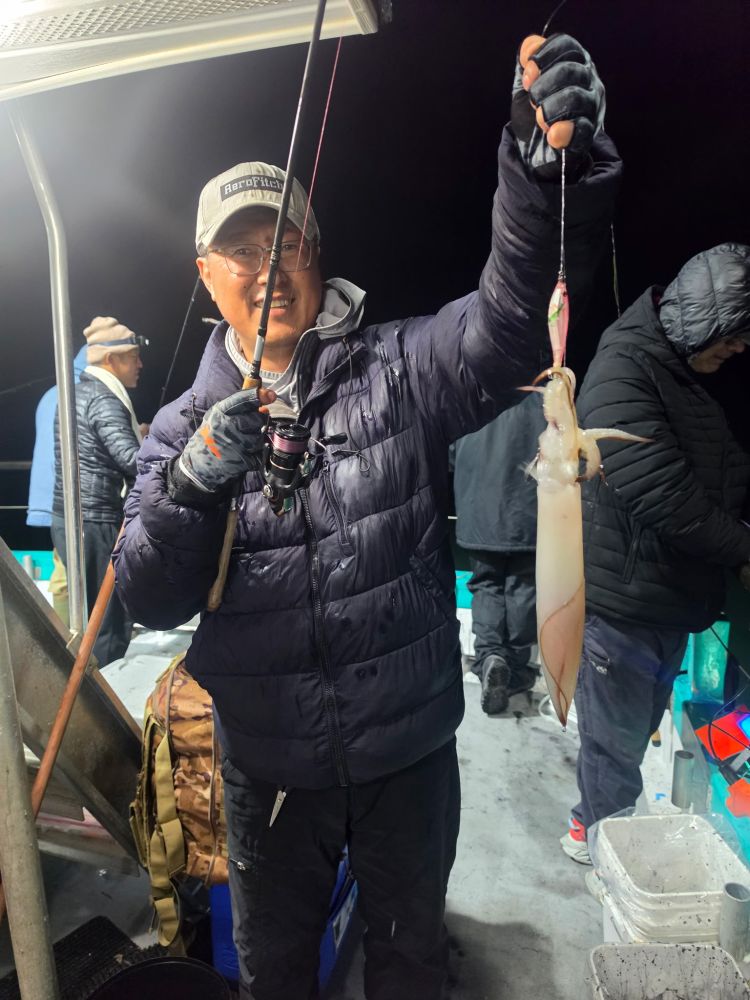 Person holding a squid on a fishing boat at night.