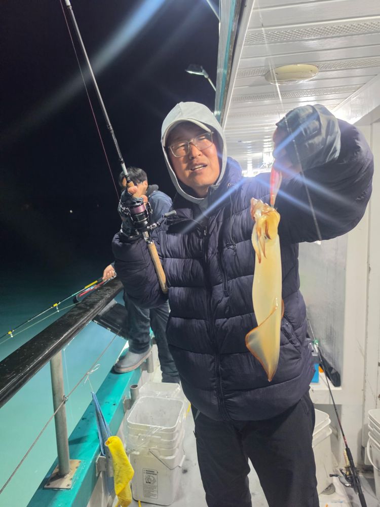 Person on a boat holding a caught squid at night.