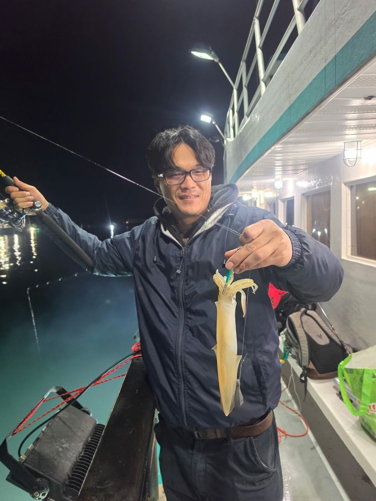 Person holding a squid on a fishing line at night on a boat.