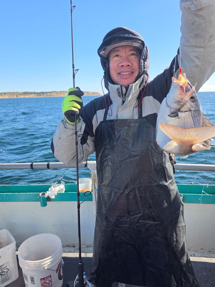 Person smiling on a boat holding a fish and fishing rod.