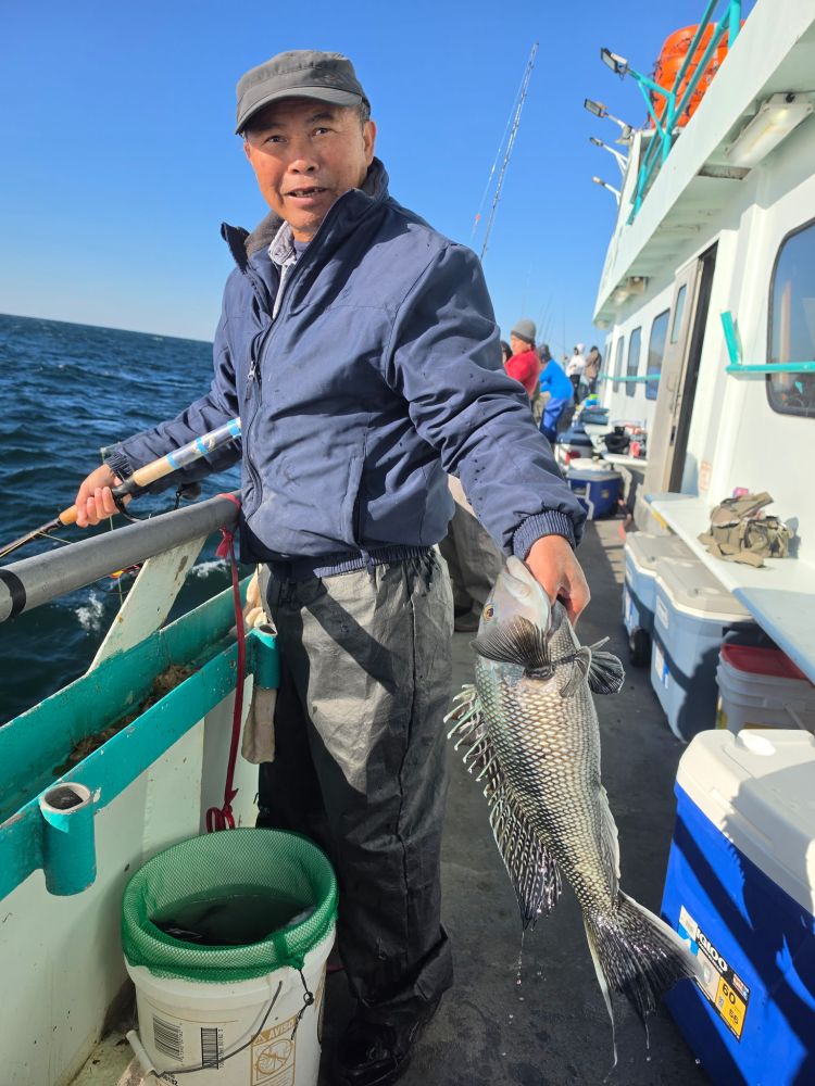 Person on a boat holding a fish, with the ocean and other people in the background.