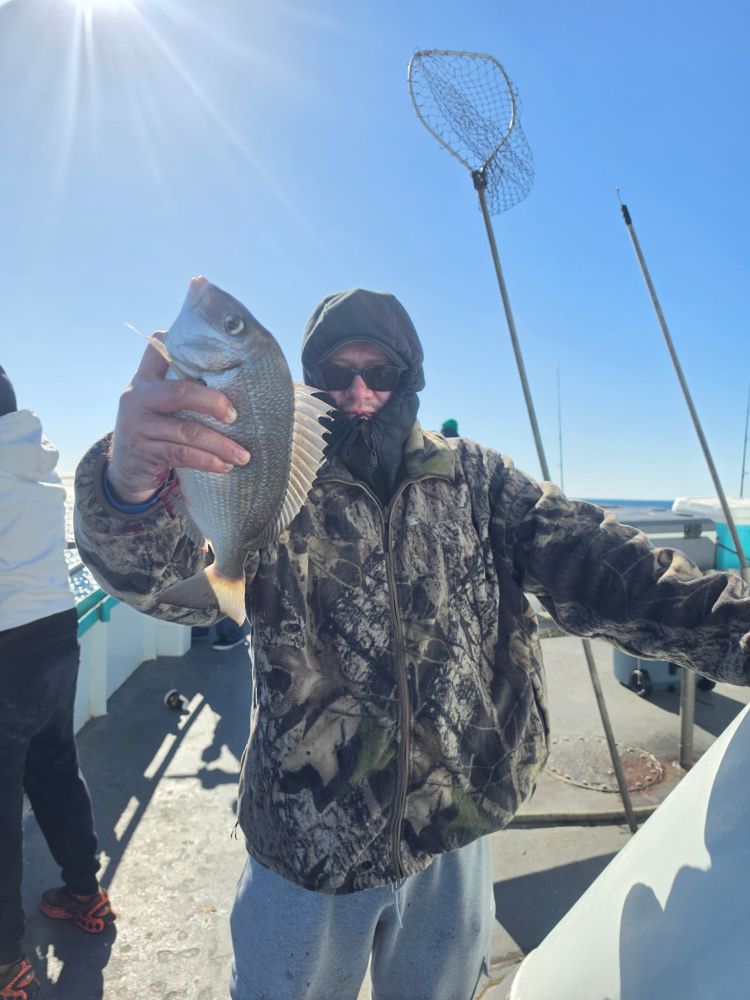 Person in camouflage holds fish on a boat with a fishing net and rods visible.