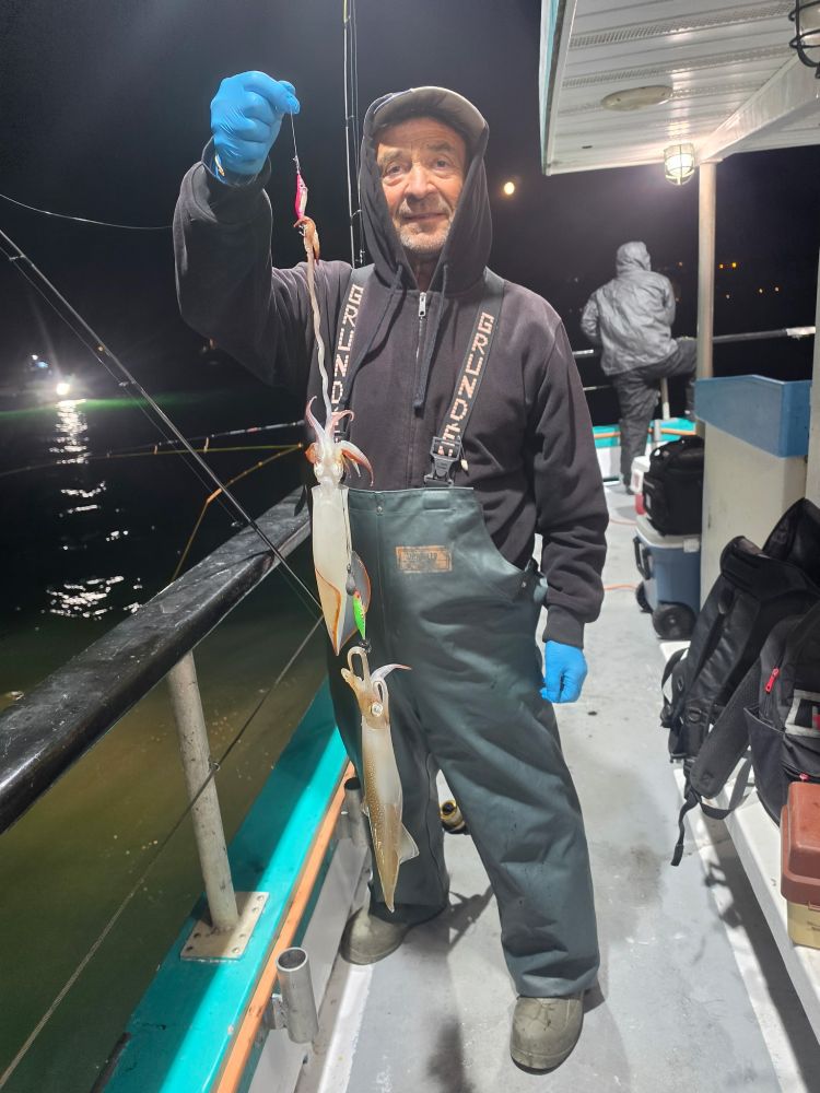 Person holding two squids on a fishing line on a boat at night.