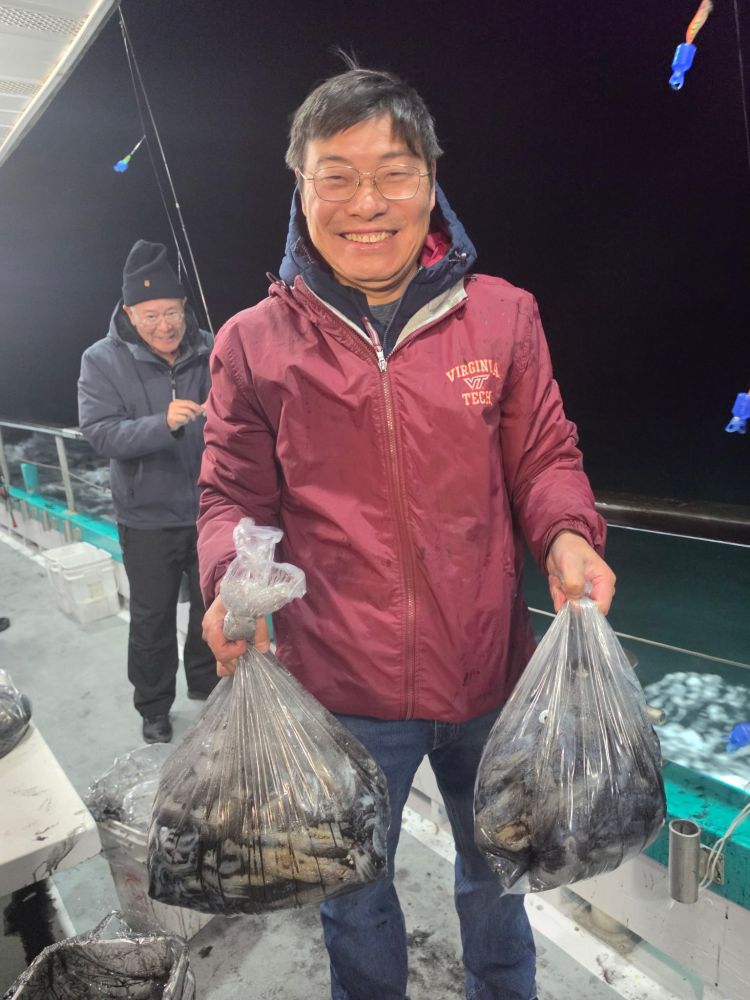 Man on boat holding bags of fish, smiling at night.