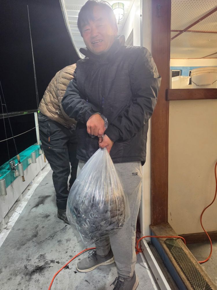Person holding a large plastic bag filled with fish on a boat deck.