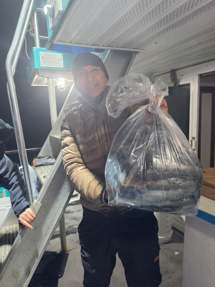 Person holding a large bag of fish on a boat at night.
