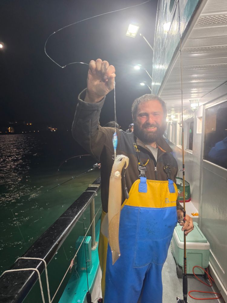 Man on boat holding a squid caught on a fishing line at night.