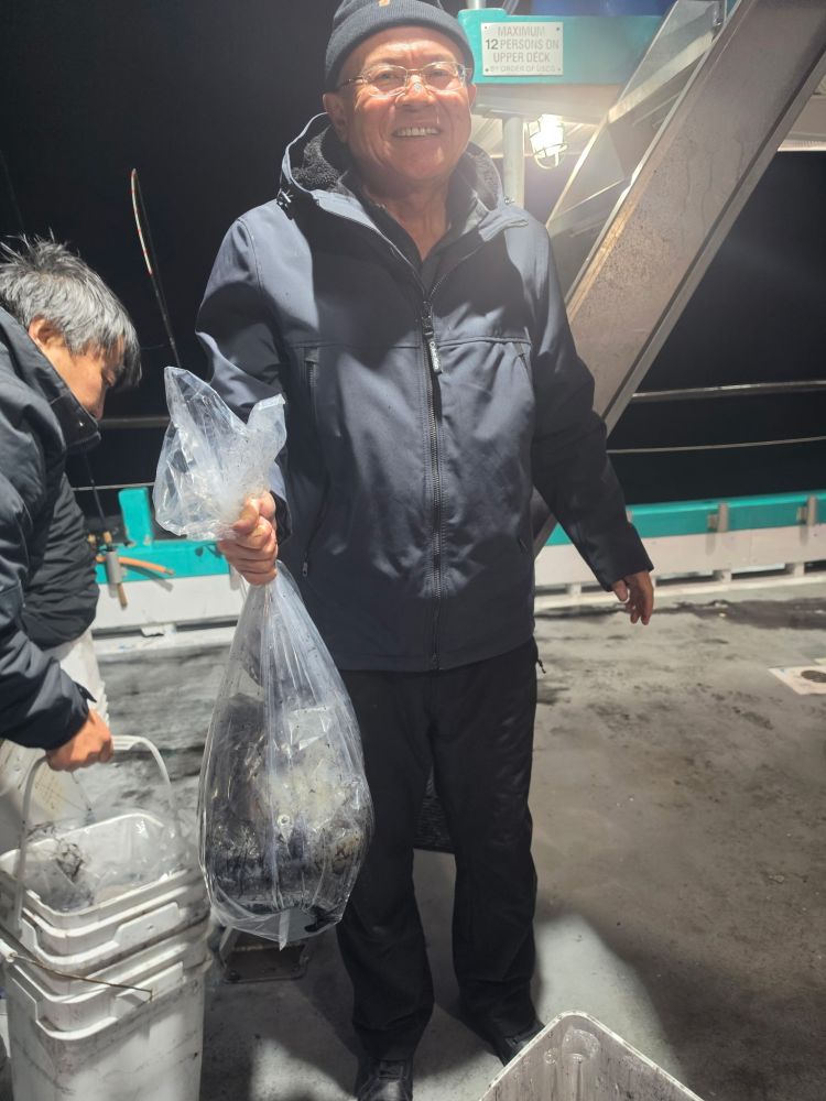Man smiling, holding a bag of fish on a boat at night.