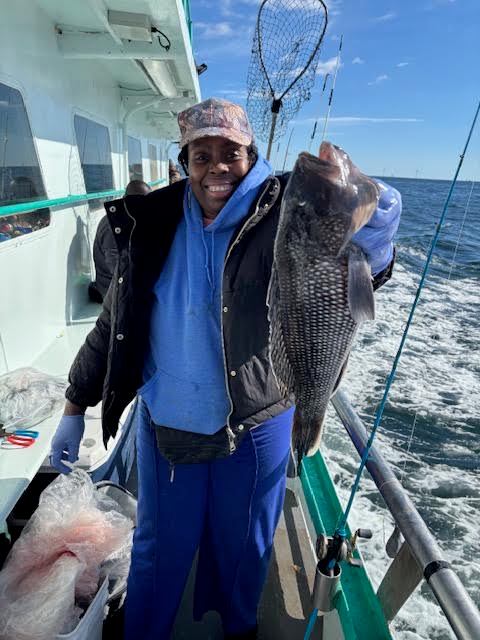 Person on boat holding a large fish, smiling, with ocean and fishing net in the background.