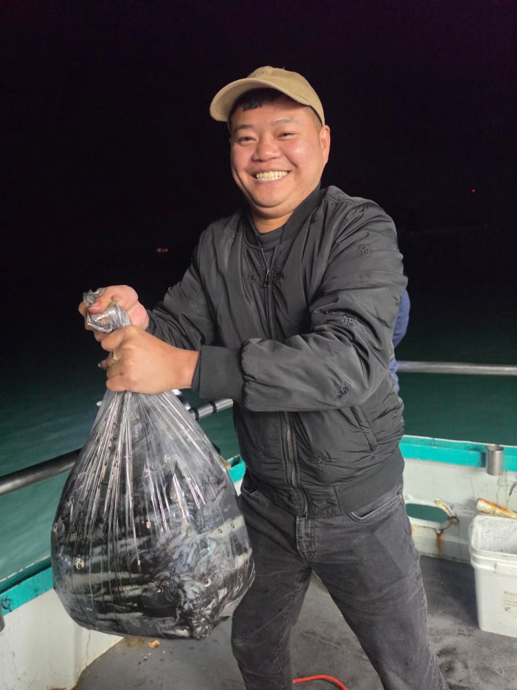 Person smiling and holding a large bag of fish on a boat at night.