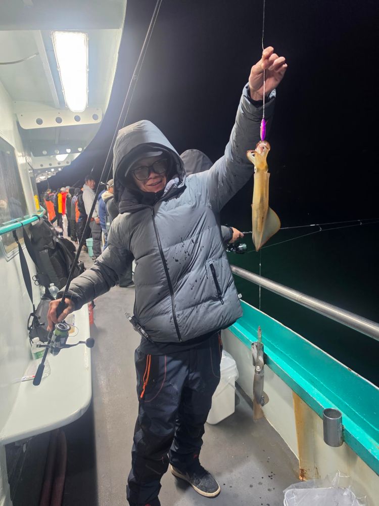 Person on a boat holding a fishing rod and a caught squid at night.