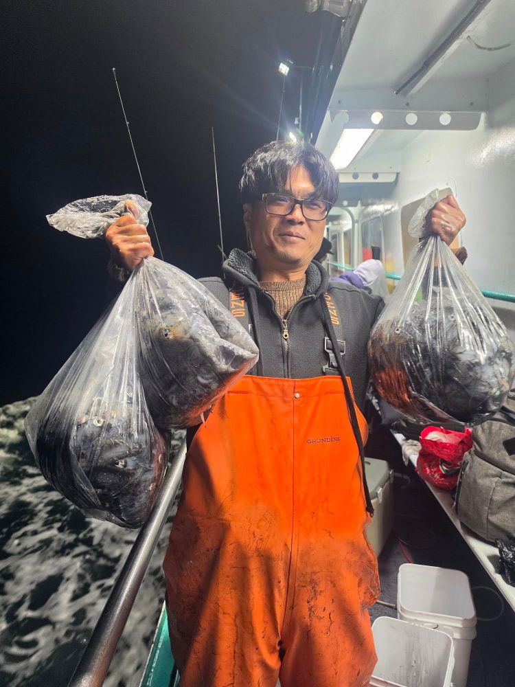 Person in orange overalls holding bags of fish on a boat at night.