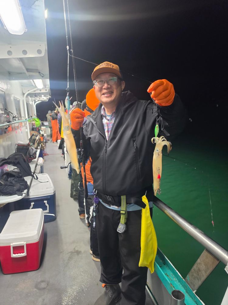 Person on a boat holding two squid at night.