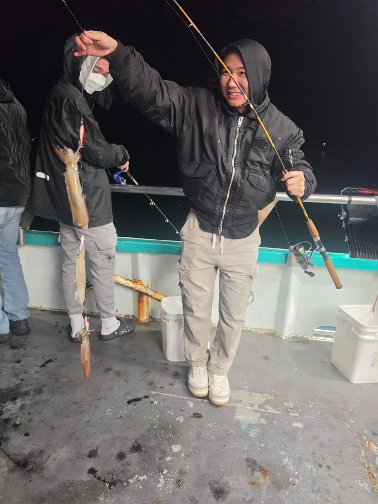 Person on boat holds fishing rod with squid catch at night.