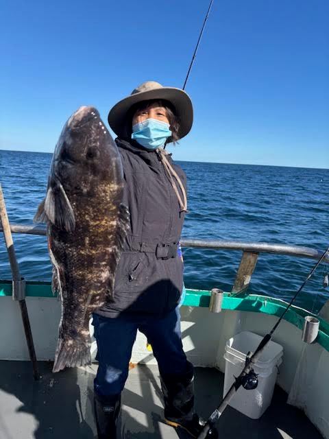 Person on a boat holding a large fish, wearing a hat and mask.