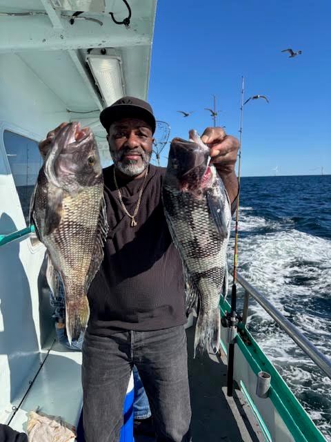 Man on boat holding two large fish with ocean background.