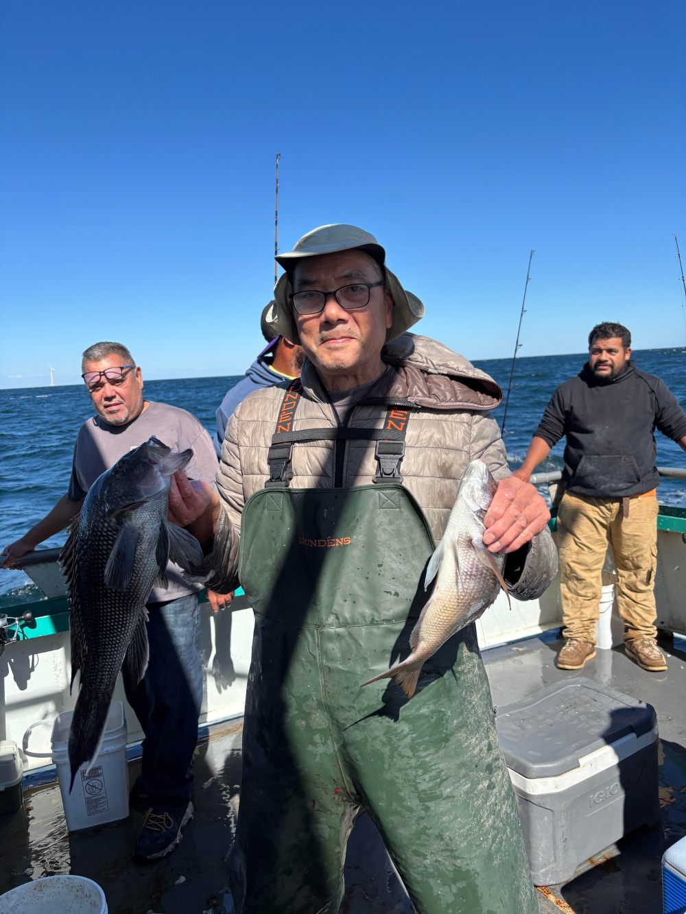 Man holding two fish on a boat with people in the background.