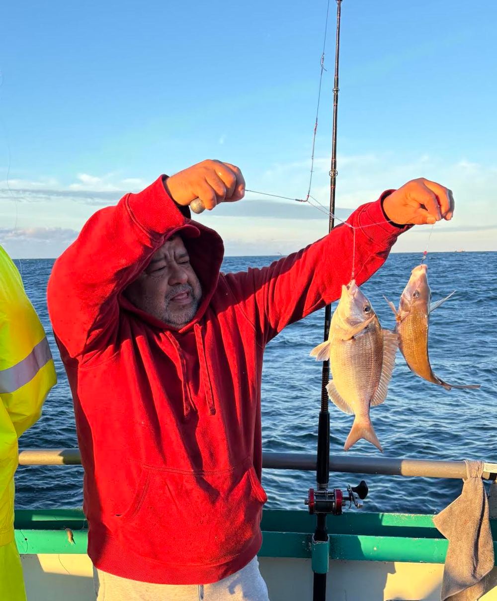 Person in red hoodie holding two fish on a boat.