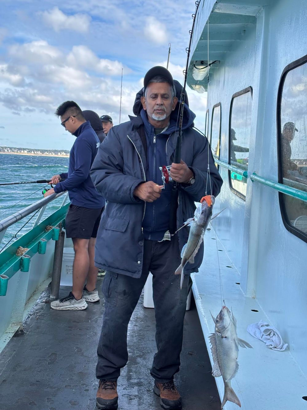 Man on boat holding fishing rod with fish, others fishing nearby.