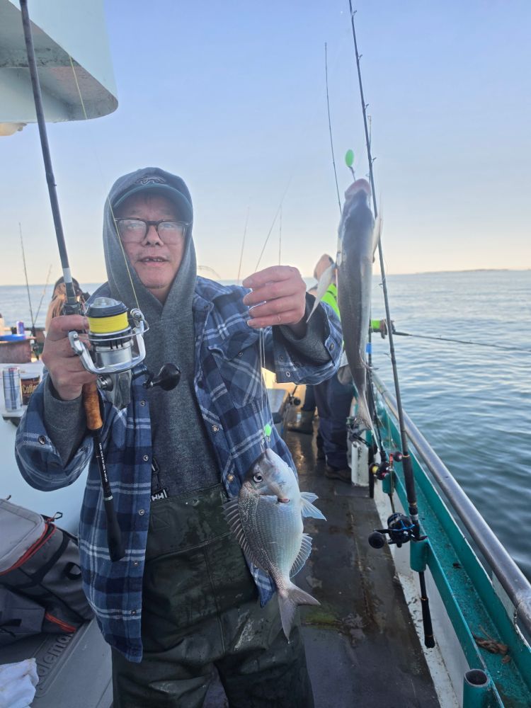 Person on boat holding a fishing rod with a fish, another person in background.