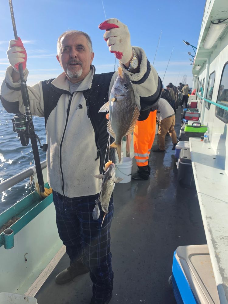 Man holding fishing rod and three fish on a boat.