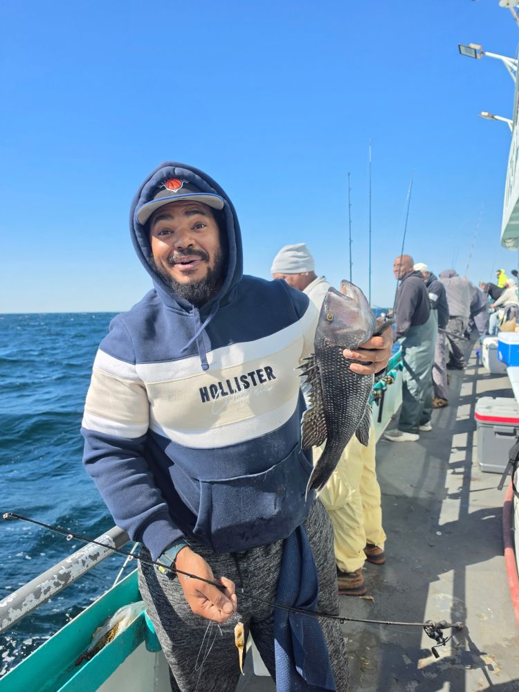 Person in hoodie holding a fish on a boat, smiling.