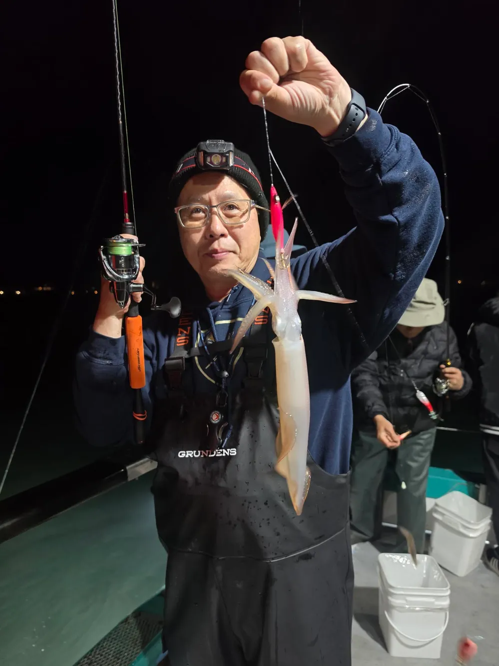 Person holding a squid while fishing at night on a boat.