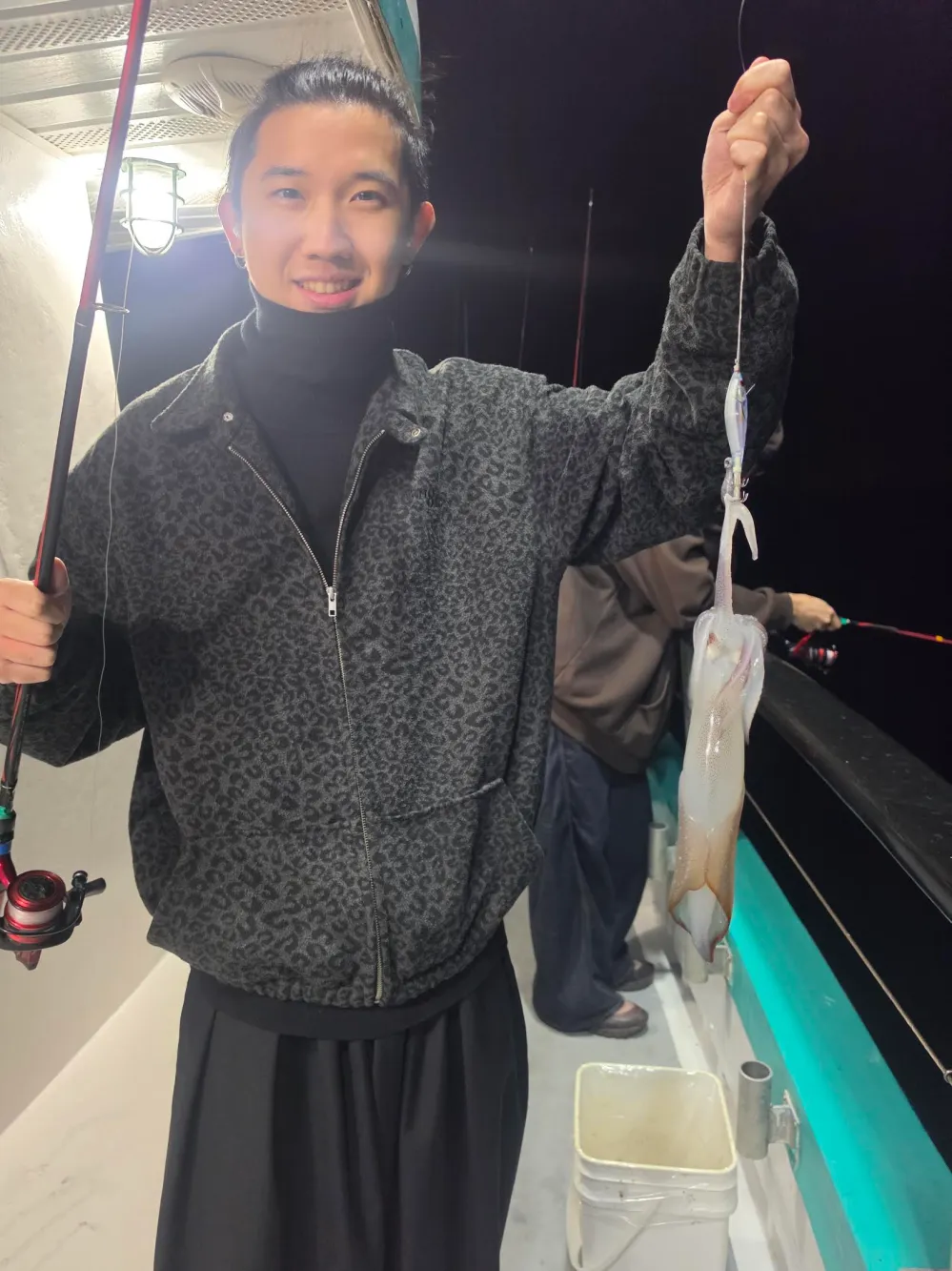 Person on a boat at night holding a caught squid.