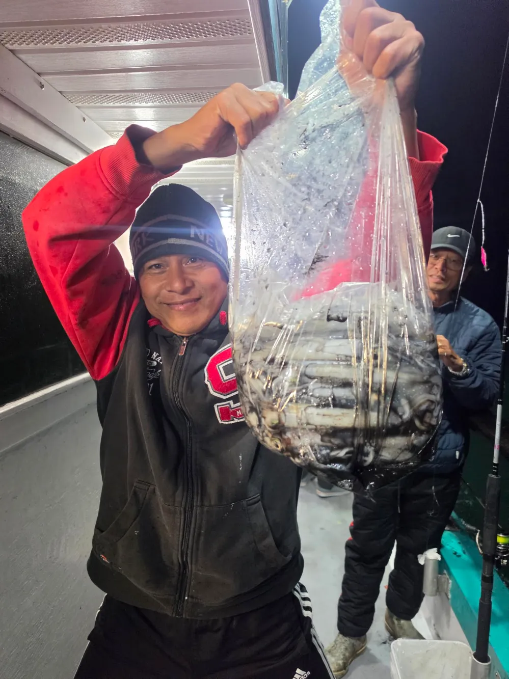 Person holding a large plastic bag filled with fish on a boat.