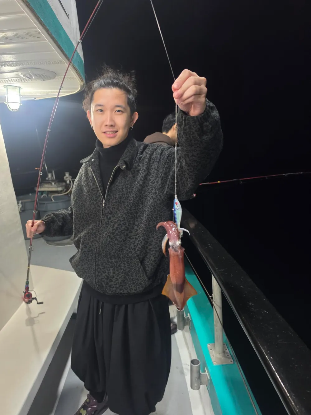 Person holding a fishing rod with a caught squid on a boat at night.
