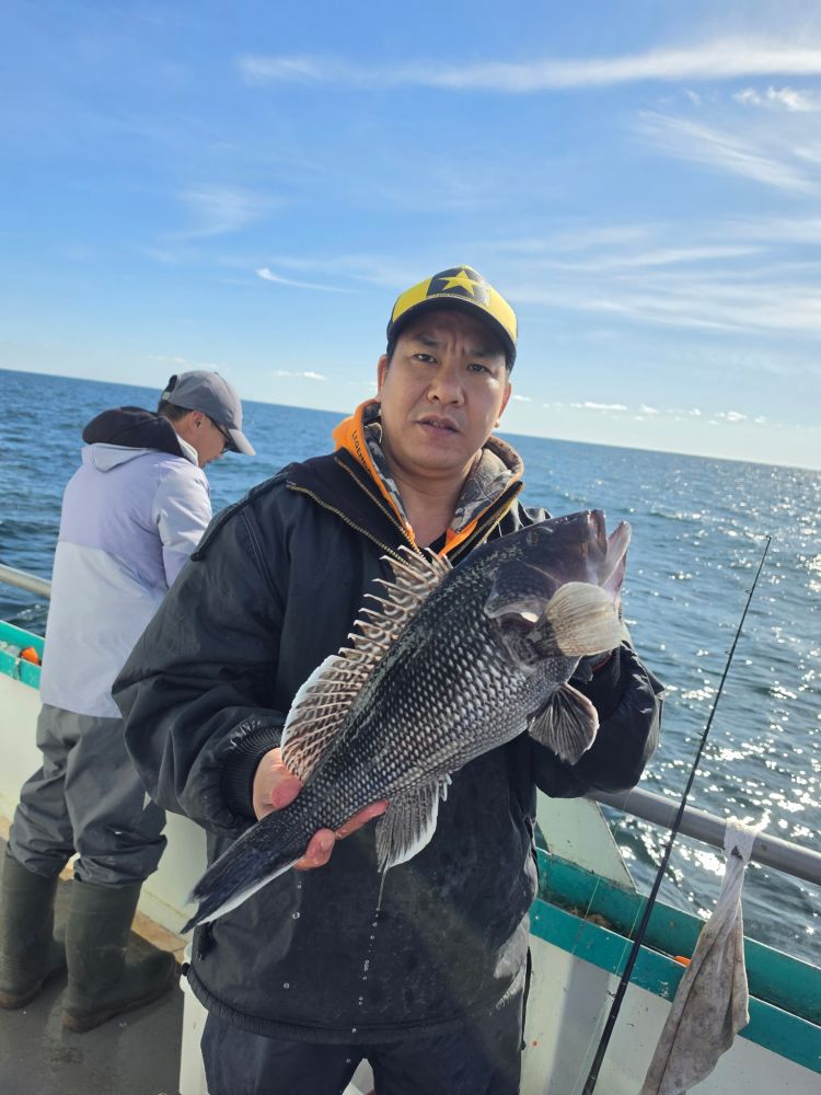 Person holding a large fish on a boat with another person and the ocean in the background.