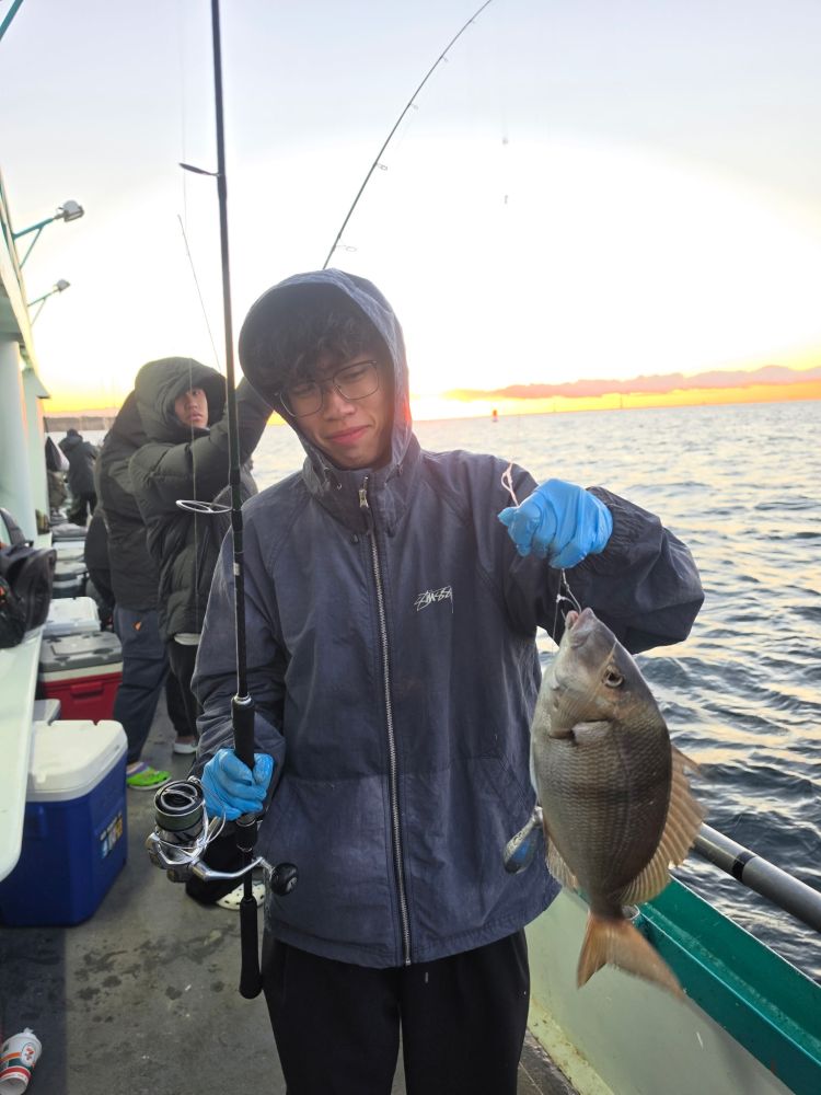 Person on boat holding a fishing rod and a fish at sunset.