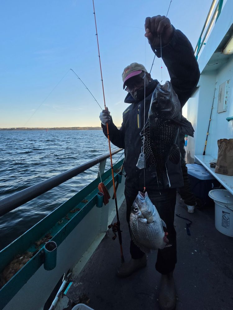 Person holding two fish on a boat, wearing a hat and mask.