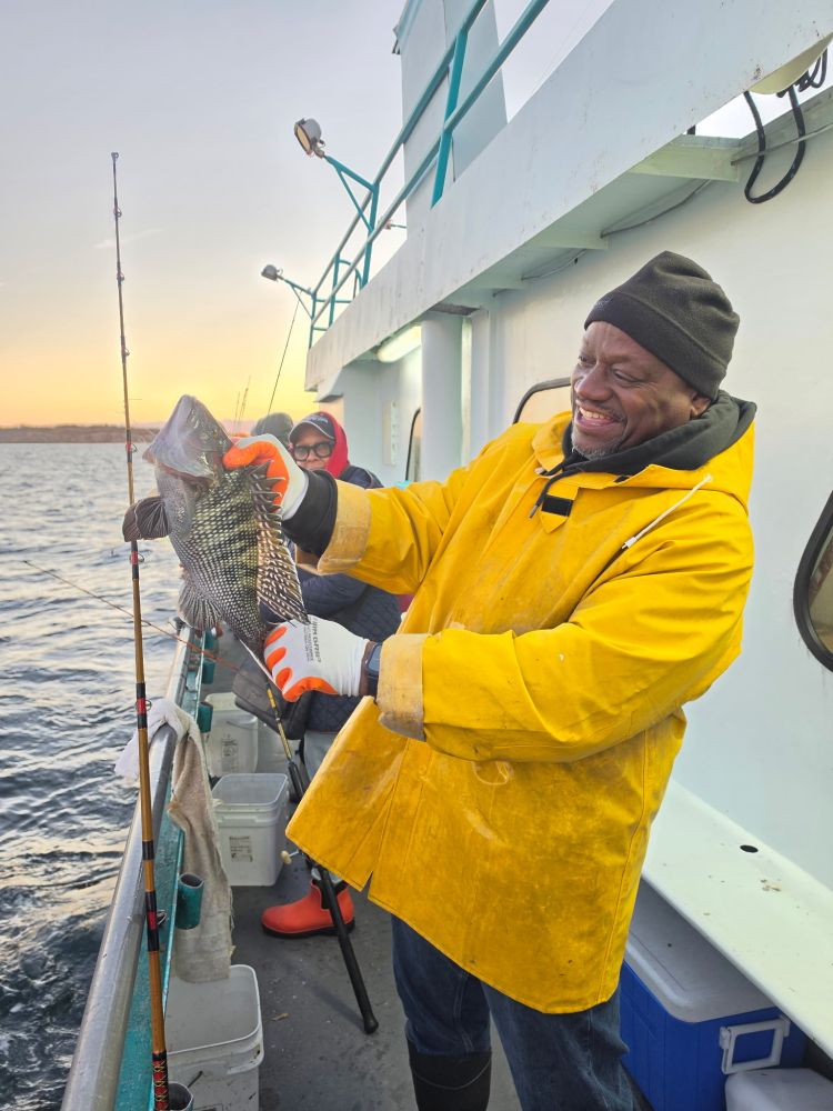 Person in yellow coat holding a fish on a boat, smiling with the ocean in the background.