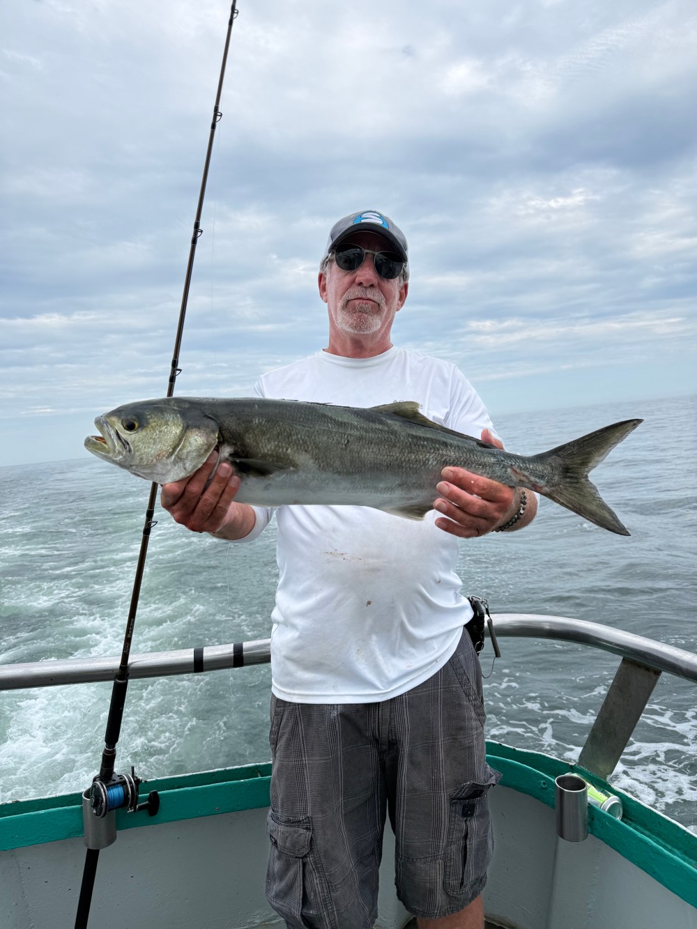 Man holding a large fish on a boat under a cloudy sky.