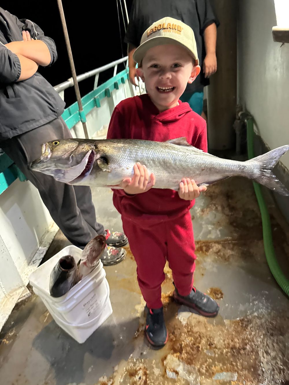 Child in red outfit smiling and holding a large fish on a boat.