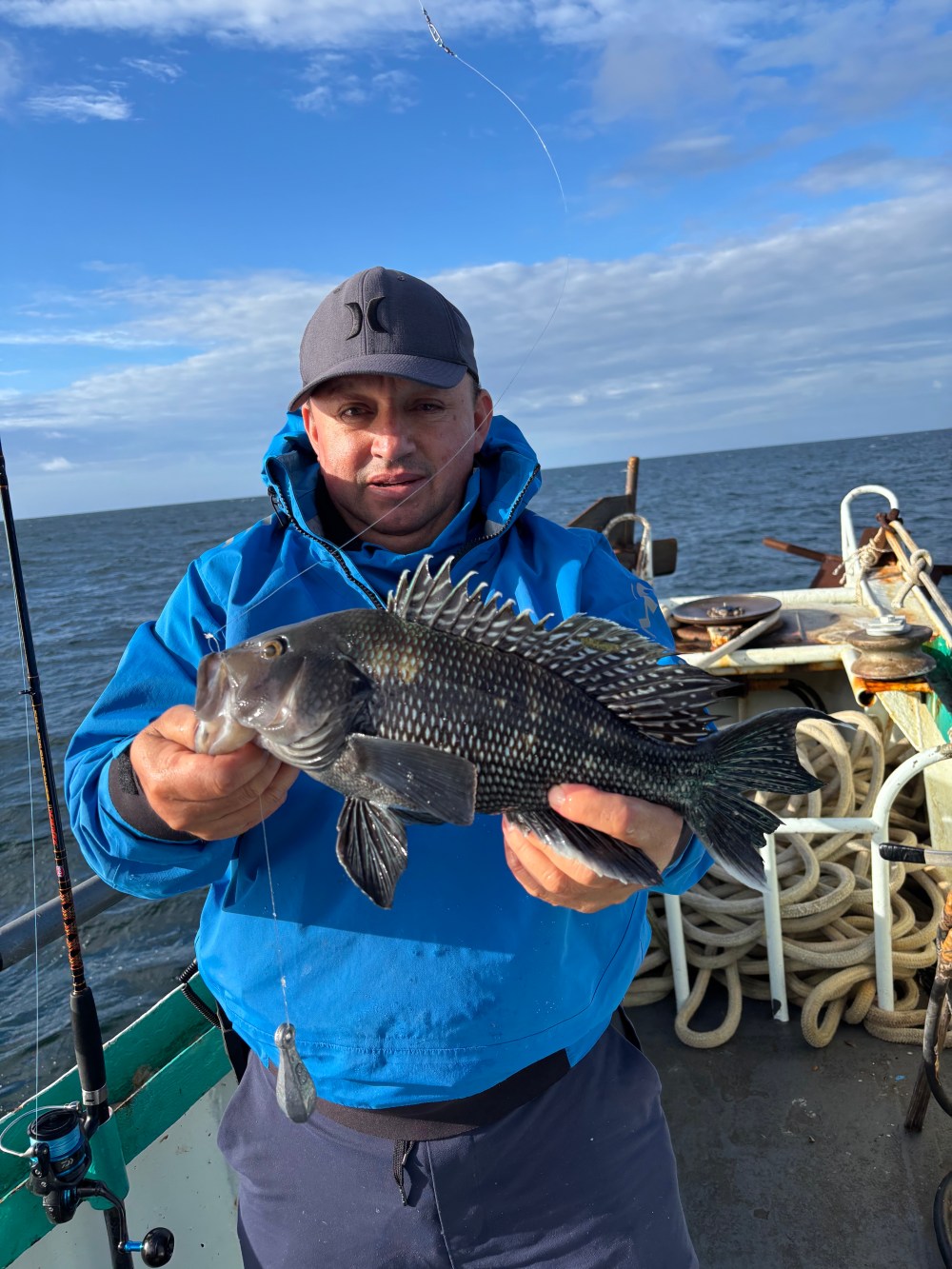 Person in blue jacket holding a fish on a boat at sea.