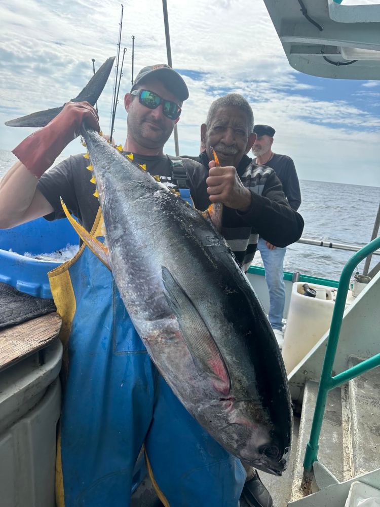Two men on a boat holding a large fish, smiling at the camera.