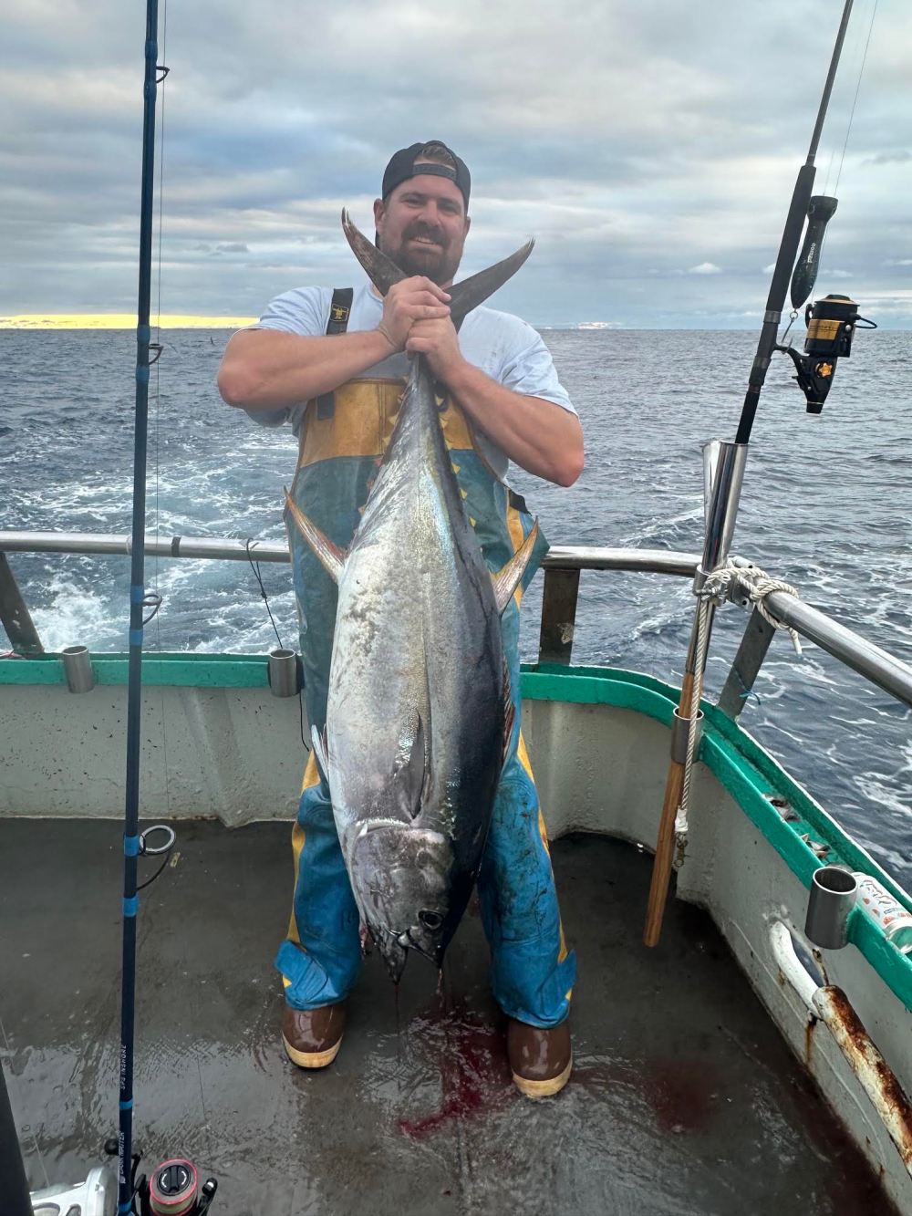 Person on a boat holding a large fish under cloudy skies.