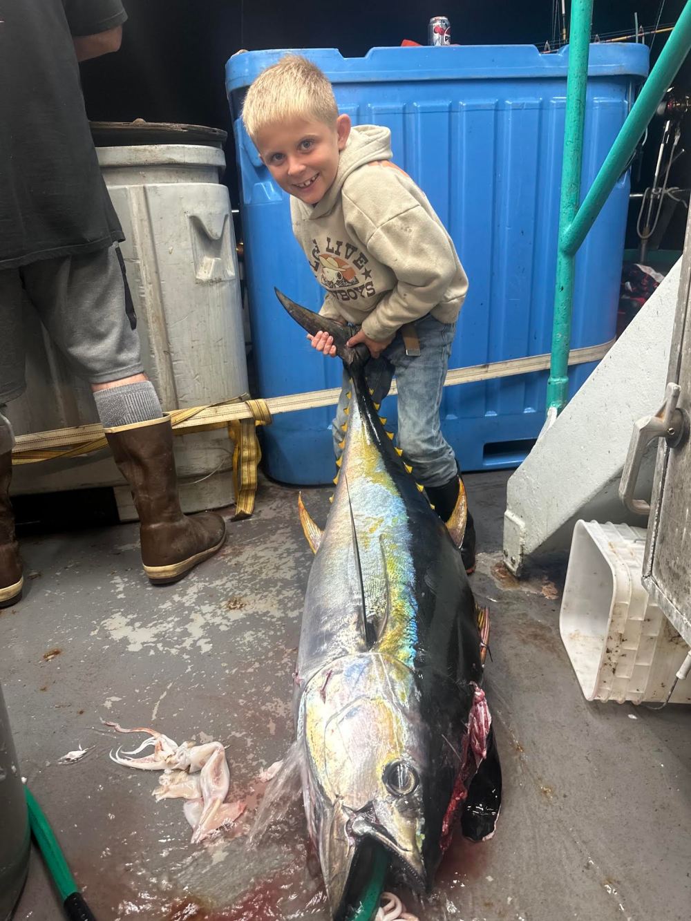 Smiling boy holding large fish on boat deck.