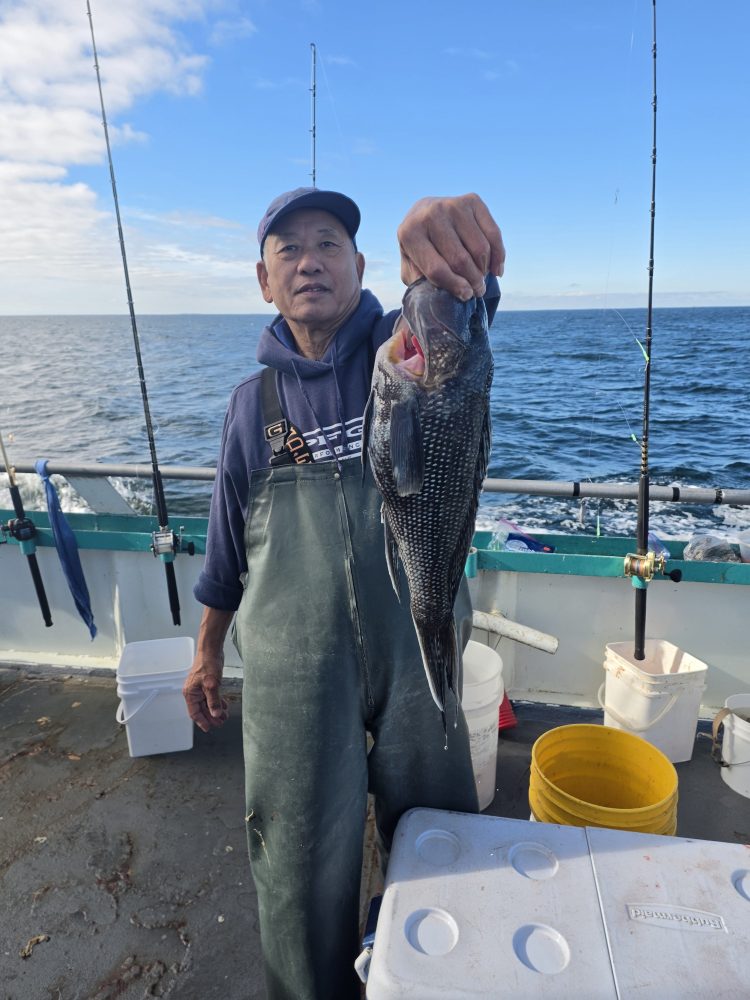 Man on boat holding a fish with ocean in the background.
